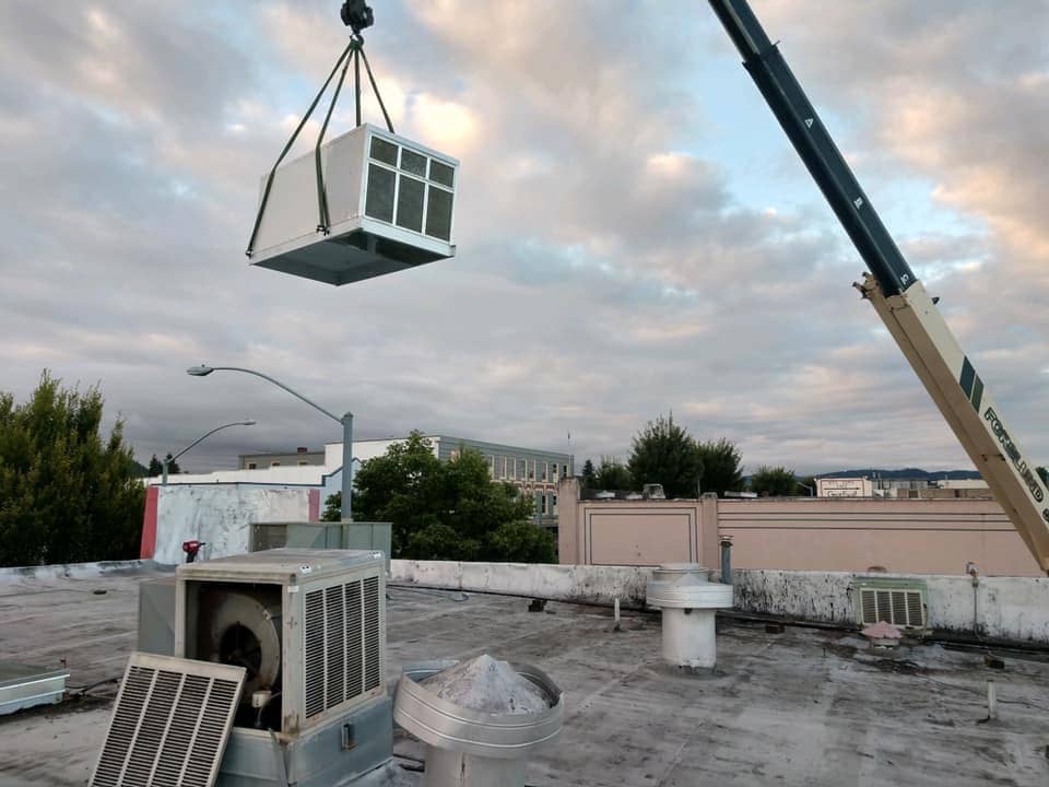 A crane lifting a HVAC unit to the roof of a building